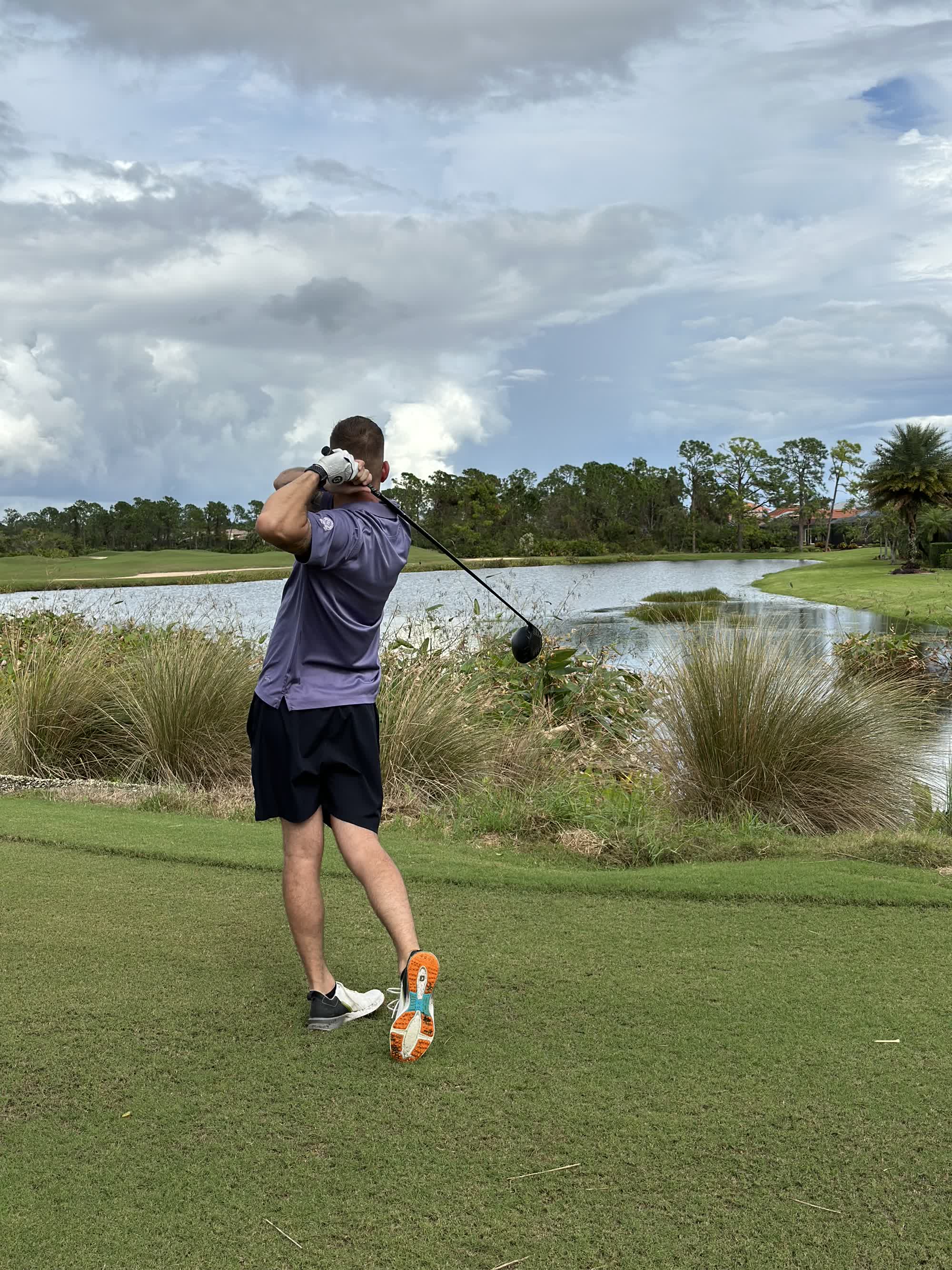 A golfer follows through on a tee shot beside a water hazard on a Florida golf course